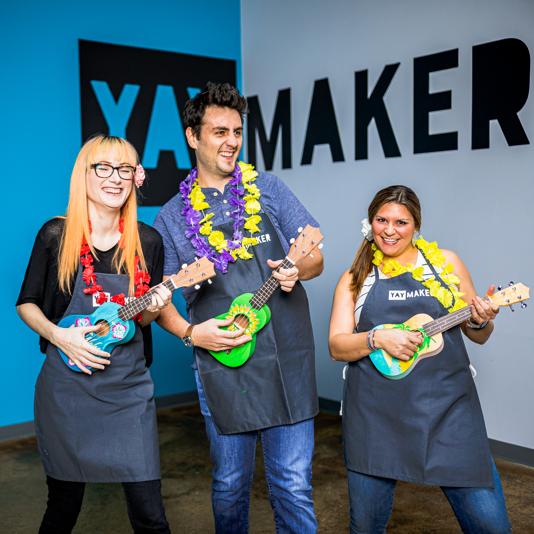 Three colleagues smiling and playing ukuleles in leis at a Yaymaker team event.